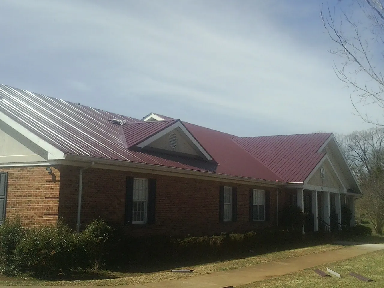 Red metal roof with gabled entries on a long brick building, from a Hail Damage Roof Repair job in Ocean Shores