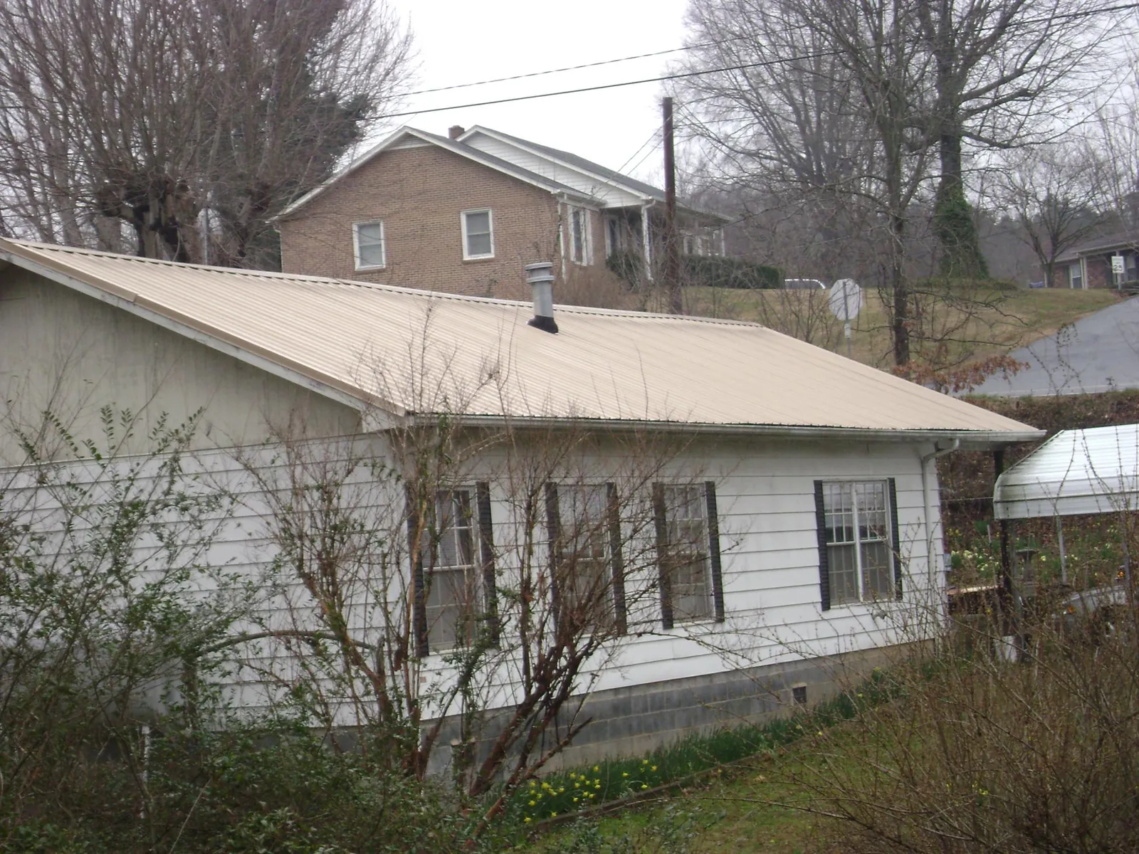 Tan metal roof on a white sided house set into a hillside — Commercial Roofing by Roofing Brothers in Ocean Shores