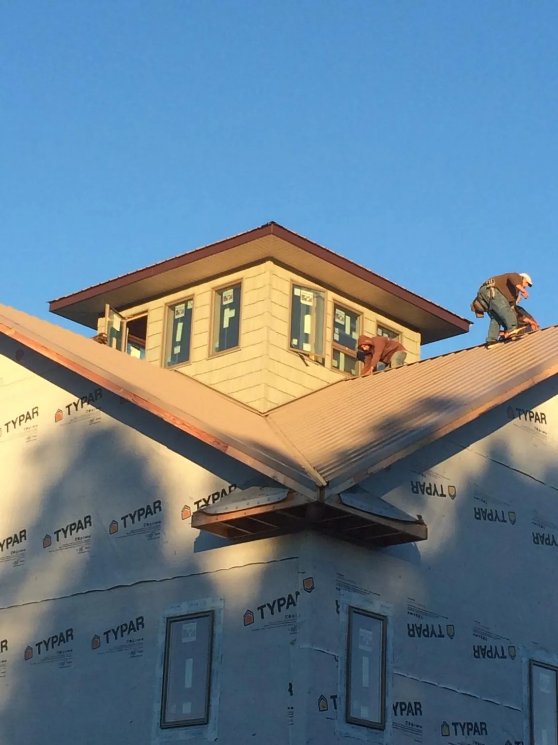 Roofers working around a rooftop cupola on a new metal roof at sunset — Roof Waterproofing in Ocean Shores by Roofing Brothers
